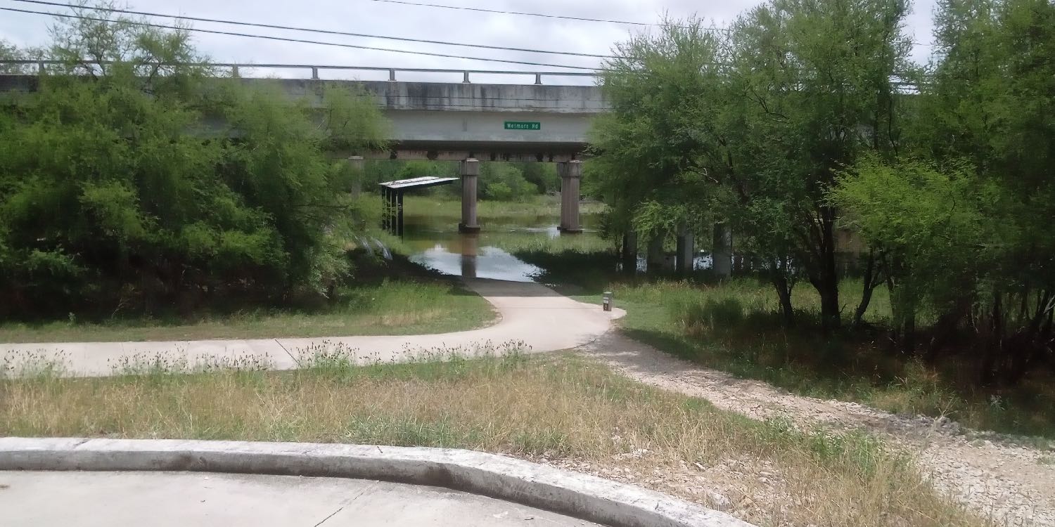 Flood waters from Salado Creek cover the greenway trail under a railroad trestle