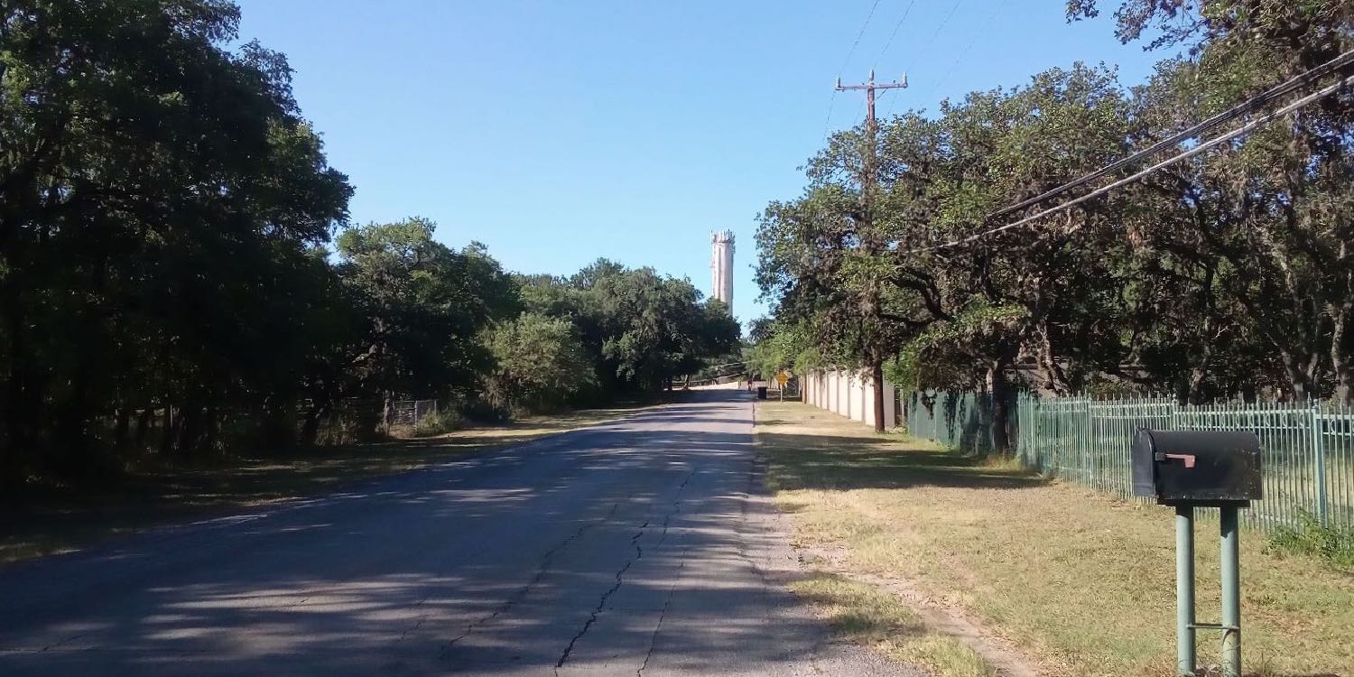 Looking south on Tower Drive, a shade-lined road with rolling hills and tall water tower on right