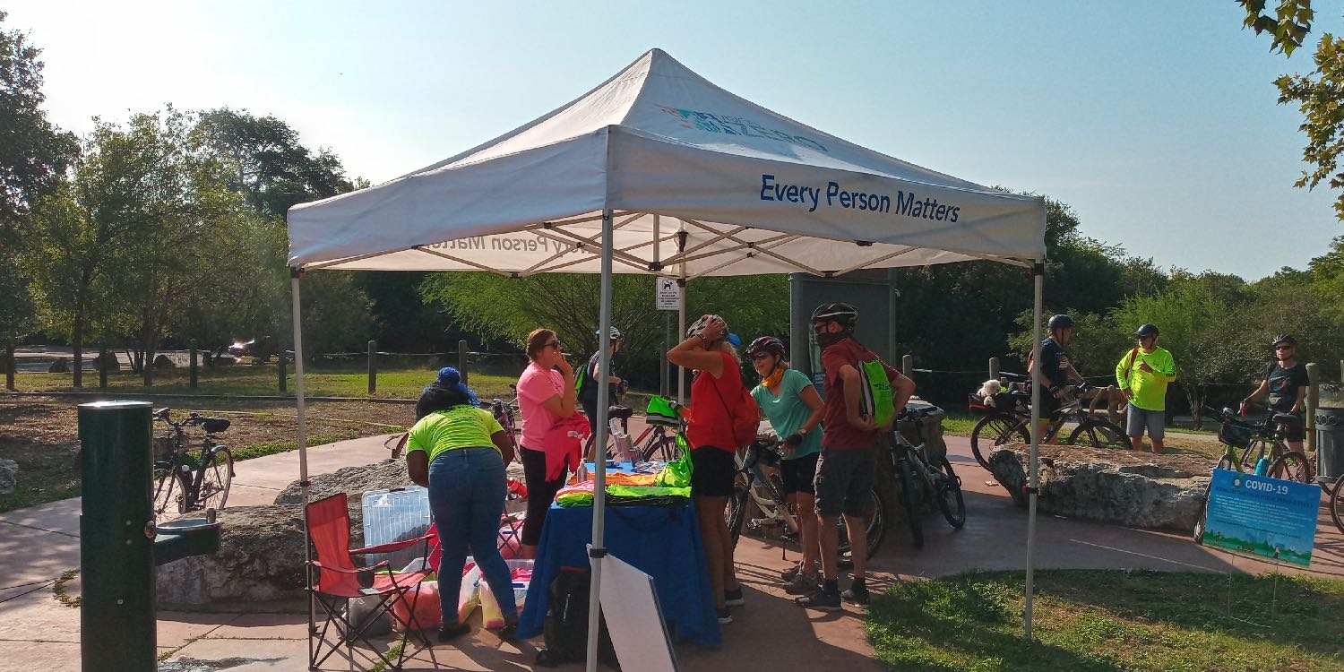 Canopy-covered booth at the Tobin Trailhead as folks gathered to receive free bright-green t-shirts, reflectors, and duffle bags