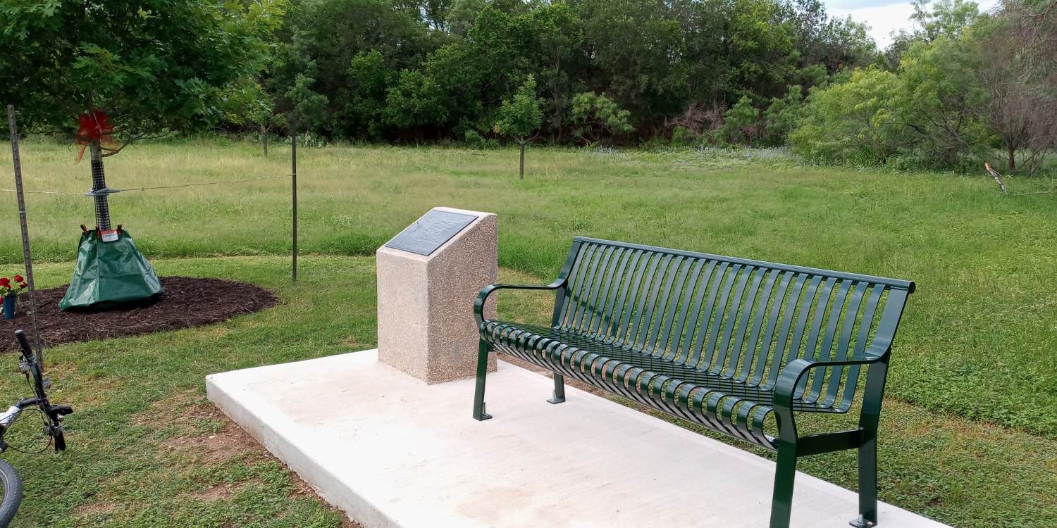 As a memorial to Rebecca Gartrell, a monument is accompanied by a bench and red oak at McAllister Park dog park trailhead
